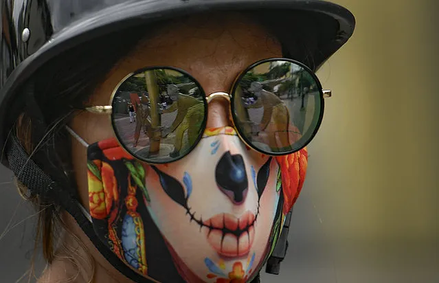 The “Oilworkers” sculpture by Beatriz Blanco is reflected in the sunglasses of a woman wearing a stylized protective face mask as a precaution against the new coronavirus, on Sabana Grande boulevard in Caracas, Venezuela, Saturday, August 1, 2020. (Photo by Matias Delacroix/AP Photo)