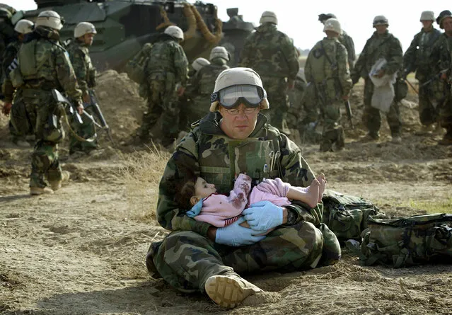 A U.S. Navy Hospital Corpsman, assigned to the 1st Marine Division, holds an Iraqi child in central Iraq, March 29, 2003. Confused front line crossfire ripped apart an Iraqi family after local soldiers appeared to force civilians towards positions held by U.S. Marines. (Photo by Damir Sagolj/Reuters)