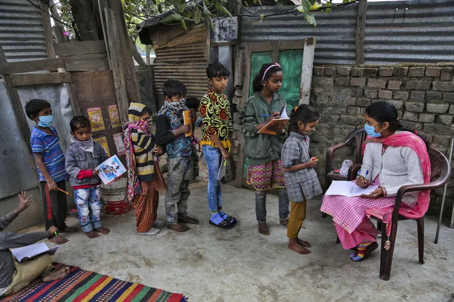 A teacher wearing face mask as a precaution against the coronavirus checks the note books of children at the Sangharsh Vidya Kendra school at a slum area on the outskirts of Jammu, India, Wednesday, November 25, 2020. The school provides free education to underprivileged children two days a week. (Photo by Channi Anand/AP Photo)