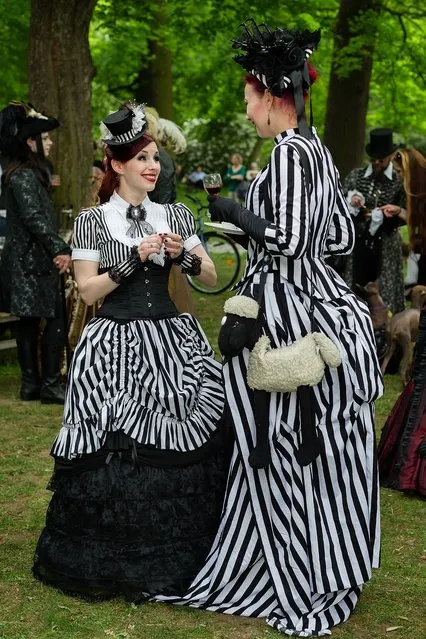 Two women in Victorian clothing and with a shawn-the-sheep-bag chat during the traditional park picnic on the first day of the annual Wave-Gotik Treffen, or Wave and Goth Festival, on May 17, 2013 in Leipzig, Germany. The four-day festival, in which elaborate fashion is a must, brings together over 20,000 Wave, Goth and steam punk enthusiasts from all over the world for concerts, readings, films, a Middle Ages market and workshops. (Photo by Marco Prosch)