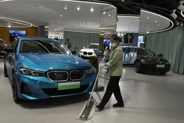 A cleaner wipes the floor near electric vehicles from BMW at a show room in Beijing, Thursday, April 13, 2023. Global and Chinese automakers plan to unveil more than a dozen new electric SUVs, sedans and muscle cars this week at the Shanghai auto show, their first full-scale sales event in four years in a market that has become a workshop for developing electrics, self-driving cars and other technology. (Photo by Ng Han Guan/AP Photo)