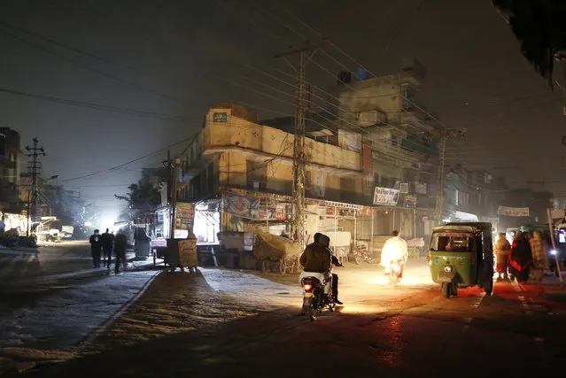 People are silhouetted on vehicles headlights on a dark street during widespread power outages in Rawalpindi, Pakistan, Sunday, January 10, 2021. Pakistan's national power grid experienced a major breakdown late night on Saturday, leaving millions of people in darkness, local media reported. (Photo by Anjum Naveed/AP Photo)