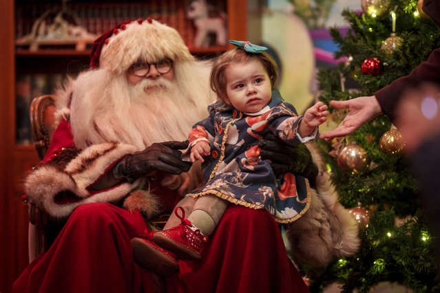 Diana, 22 months old, reaches for her mother's hand as she poses with a man wearing a Santa Claus outfit at Christmas fair in Bucharest, Romania, Saturday, December 14, 2024. (Photo by Vadim Ghirda/AP Photo)