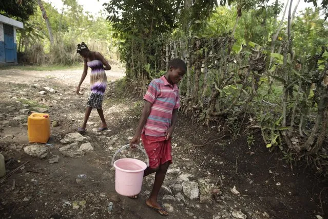 Siblings Mylouise Veillard, left, and Myson walk home with water they collected from a well, for cooking, cleaning and drinking, in a rural area of Saint-Louis-du-Sud, Haiti, Thursday, May 25, 2023. The siblings were considered “poverty orphans” for three years until they were reunited with their mother, Renèse Estève, who had dropped them off at an orphanage where she believed they'd get better care. Their mother brought them home after she was startled at the weight they had lost, convinced they'd be better off living in grinding poverty. (Photo by Joseph Odelyn/AP Photo)