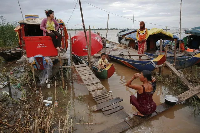 Ethnic Cham Muslim people pass the time near their boats on banks of Mekong river in Phnom Penh July 29, 2013. About 100 ethnic Cham families, made up of nomads and fishermen without houses or land who arrived at the Cambodian capital in search of better lives, live on their small boats on a peninsula where the Mekong and Tonle Sap rivers meet, just opposite the city's centre. The community has been forced to move several times from their locations in Phnom Penh as the land becomes more valuable. They fear that their current home, just behind a new luxurious hotel under construction at the Chroy Changva district is only temporary and that they would have to move again soon. (Photo by Damir Sagolj/Reuters)