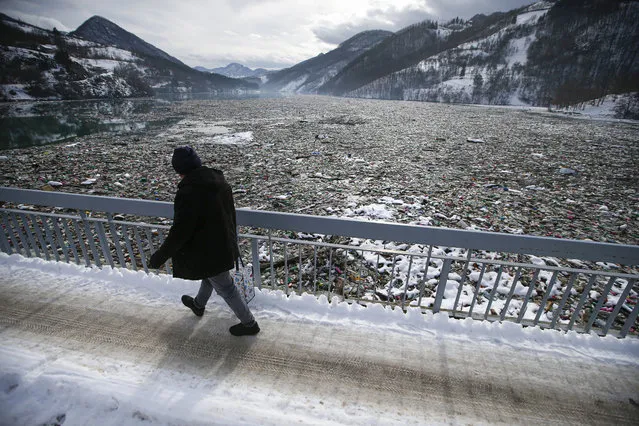 A man walks by tons of garbage stuck at the foot of the hydro power plant at the Potpecko accumulation lake near Priboj, in southwest Serbia, Friday, January 22, 2021. Serbia and other Balkan nations are virtually drowning in communal waste after decades of neglect and lack of efficient waste-management policies in the countries aspiring to join the European Union. (Photo by Darko Vojinovic/AP Photo)