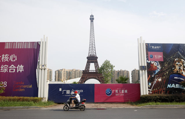 A man rides his motorcycle past a replica of the Eiffel Tower at the Tianducheng development in Hangzhou, Zhejiang Province August 1, 2013. Tianducheng, developed by Zhejiang Guangsha Co. Ltd., started construction in 2007 and was known as a knockoff of Paris with a scaled replica of the Eiffel Tower standing at 108 metres (354 ft) and Parisian houses. Although designed to accommodate at least 10 thousand people, Tianducheng remains sparsely populated and is now considered as a “ghost town”, according to local media. (Photo by Aly Song/Reuters)