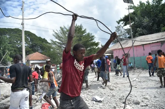 Haitian people collect metal on October 7, 2018 in Gros Morne, Haiti, from the destroyed auditorium, after the earthquake that struck north of Haiti, on October 6, 2018. A body was rescued after a 5.9-magnitude earthquake struck off the northwest coast of Haiti late Saturday, killing at least 11 people, injuring more than 130 others and damaging homes in the Caribbean nation, authorities said. The epicenter of the quake was located about 19 kilometers (12 miles) northwest of the city of Port-de-Paix, the US Geological Survey reported. (Photo by Hector Retamal/AFP Photo)