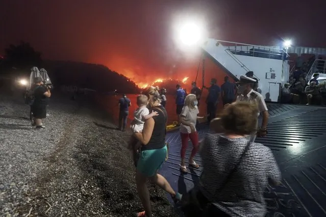 People embark a ferry during an evacuation from Kochyli beach as wildfire approaches near Limni village on the island of Evia, about 160 kilometers (100 miles) north of Athens, Greece, Friday, August 6, 2021. Thousands of people fled wildfires burning out of control in Greece and Turkey on Friday, including a major blaze just north of the Greek capital of Athens that claimed one life, as a protracted heat wave left forests tinder-dry and flames threatened populated areas and electricity installations. (Photo by Thodoris Nikolaou/AP Photo)