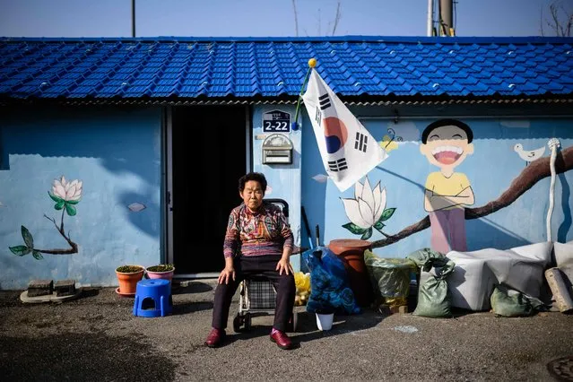 An elderly woman rests her eyes while sitting in front of a mural outside a property in Dongducheon, Gyeonggi Province, about 38 kilometers north of Seoul, on November 22, 2023. (Photo by Anthony Wallace/AFP Photo)