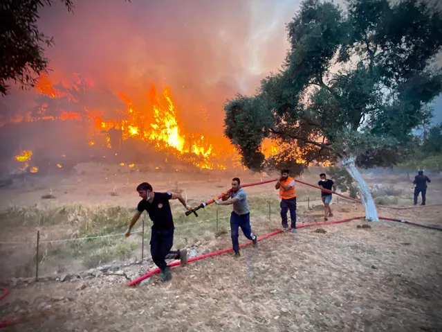 Firemen and local volunteers carry hosepipes as they fight to extinguish a wildfire in Oren, in the holiday region of Mugla, on August 6, 2021 as Turkey struggles against its deadliest wildfires in decades. Greece and Turkey have been fighting blaze upon blaze over the past week, hit by the worst heatwave in decades, a disaster that officials and experts have linked to increasingly frequent and intense weather events caused by climate change. (Photo by Serdar Gurbuz/AFP Photo)