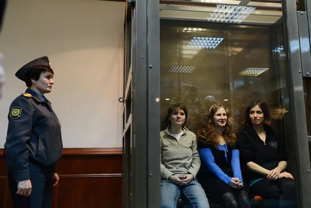 A police officer guards members of the all-girl punk band “p*ssy Riot” (L-R) Yekaterina Samutsevich, Maria Alyokhina and Nadezhda Tolokonnikova sitting in a glass-walled cage in a court in Moscow, on October 10, 2012. (Photo by Natalia Kolesnikova/AFP Photo)