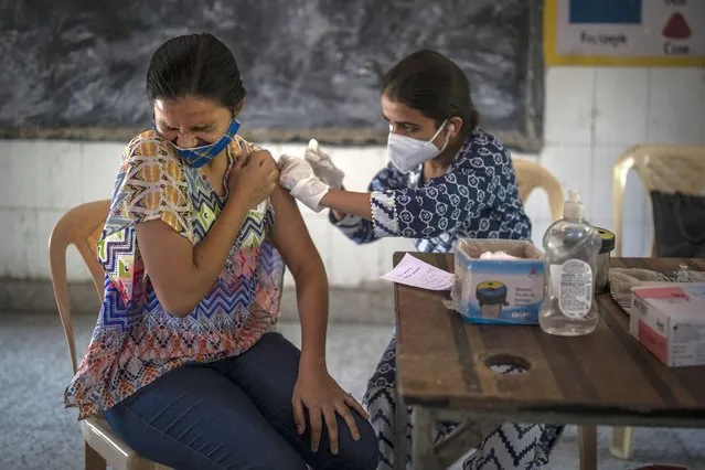 A woman reacts as a health worker inoculates her during a vaccination drive against coronavirus inside a school in New Delhi, India, Wednesday, October 20, 2021. India is nearing a milestone of administering a total of one billion doses against COVID-19. (Photo by Altaf Qadri/AP Photo)