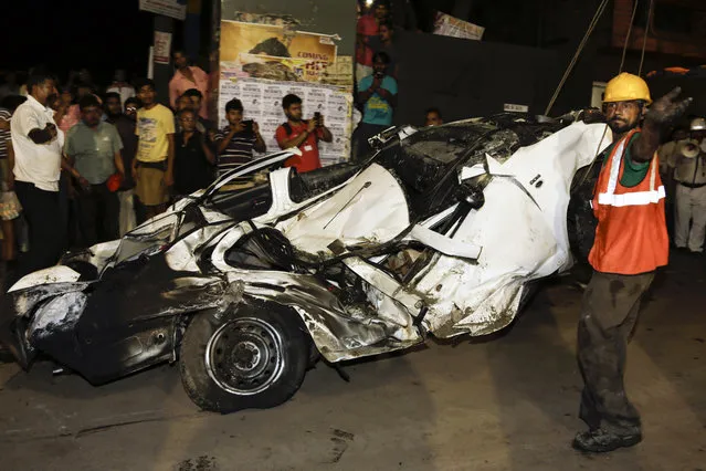 An Indian rescue worker gestures beside a mangled car recovered from a partially collapsed overpass in Kolkata, India, Thursday, March 31, 2016. A long section of a road overpass under construction collapsed Wednesday in a crowded Kolkata neighborhood, with tons of concrete and steel slamming into midday traffic, killing several and injuring many. (Photo by Bikas Das/AP Photo)