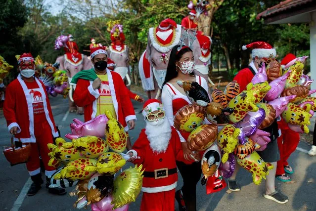 People in Santa Claus costumes walk during the visit of five elephants wearing Santa Claus costumes with giant face masks, delivering hand sanitizers and promoting a “get vaccinated” message to a primary school in the historical city of Ayutthaya, Thailand, December 24, 2021. (Photo by Soe Zeya Tun/Reuters)
