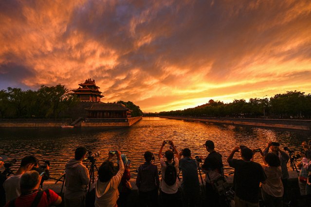 People take photos of a corner tower near the Forbidden city during sunset in Beijing on May 14, 2024. (Photo by Jade Gao/AFP Photo)
