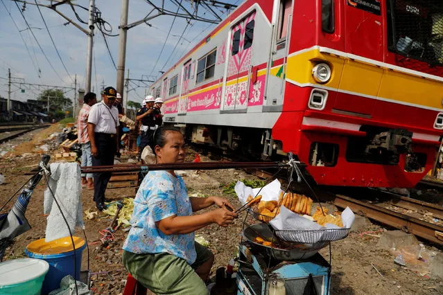 A vendor (R) prepares food at a vegetable market as a commuter train passes by in Jakarta, Indonesia, May 4, 2016. (Photo by Reuters/Beawiharta)