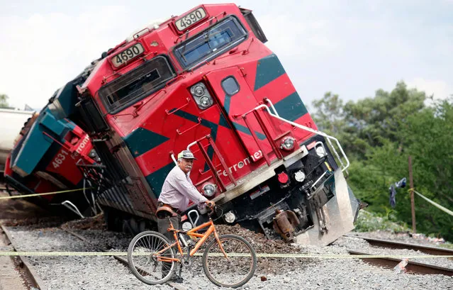 A man with a bicycle passes by a train which derailed in the community of San Isidro Mazatepec in Tala, State of Jalisco, Mexico, on June 15, 2021. A freight train derailed and toppled onto houses alongside the tracks in western Mexico on Tuesday, killing one resident and injuring three others, emergency services said. Two locomotives and 12 train cars overturned in the town of San Isidro Mazatepec in the state of Jalisco, the region's civil protection and fire department said on Twitter. (Photo by Ulises Ruiz/AFP Photo)