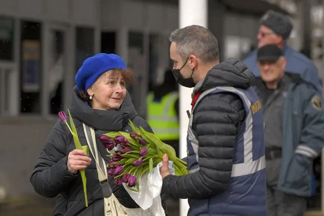 A Romanian Immigrations officer gives flowers to a refugee fleeing the conflict from neighbouring Ukraine after she crossed the border on International Women's Day, at the Romanian-Ukrainian border, in Siret, Romania, Tuesday, March 8, 2022. It is a global day to celebrate women, but many fleeing Ukraine feel only the stress of finding a new life for their children as husbands, brothers and fathers stay behind to defend their country from Russia's invasion. (Photo by Andreea Alexandru/AP Photo)