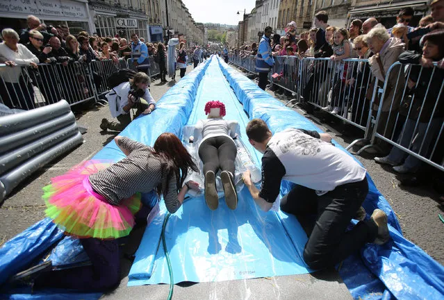 A participant on a lilo slides down a giant water slide that has been installed down Park Street on May 4, 2014 in Bristol, England. The 90m (295ft) slide was made from plastic sheets, hay bales, water and washing-up liquid and was the brainchild of artist Luke Jerram. The three hundred ticket holders who were picked from nearly 100,000 applicants took turns to hurtle down the slide watched by hundreds of spectators lining the street that was closed to traffic. (Photo by Matt Cardy/Getty Images)