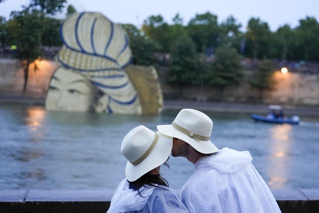 A couple kiss while waiting for team boats to pass on the Seine in Paris, France, during the opening ceremony of the 2024 Summer Olympics, Friday, July 26, 2024. (Photo by Rebecca Blackwell/AP Photo)