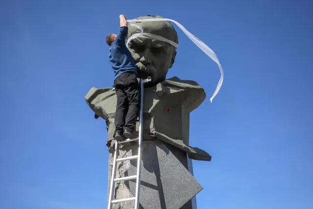 An activist display symbolically bandages on shrapnel holes in the head of the monument of Ukrainian poet, writer, artist, public and political figure Taras Shevchenko in the town of Borodianka, northwest of Kyiv, on April 7, 2022, during Russia's military invasion launched on Ukraine. (Photo by Aleksey Filippov/AFP Photo)