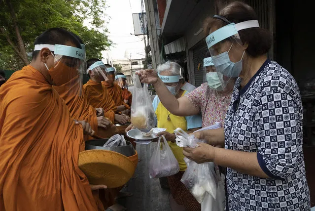 Devotees offer food to Thai Buddhist monks as they wear face shield to protect themselves from new coronavirus in Bangkok, Thailand, Tuesday, March 31, 2020. (Photo by Sakchai Lalit/AP Photo)