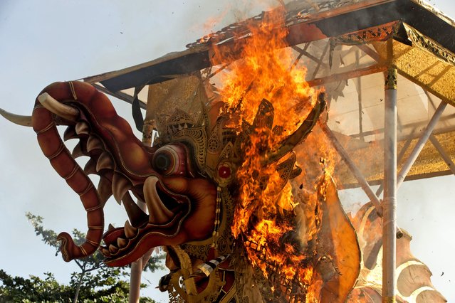 Fire engulfs a giant effigy of a mythical animal containing the remains of 117 people during a traditional mass cremation called “ngaben” on Friday, July 29, 2022, in Padangbai, Bali, Indonesia. The previously buried remains were dug up and placed in a temporary shrine before being cremated. Balinese believe that cremating the dead liberates their souls, allowing them to enter the higher world to reincarnate into better beings. (Photo by Firdia Lisnawati/AP Photo)