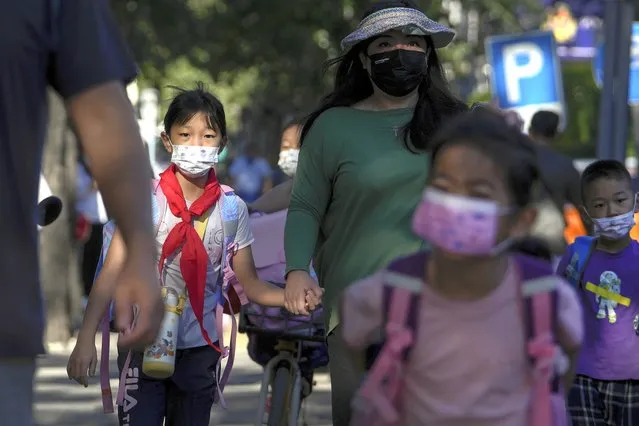 Students wearing face masks are accompanied by their relatives as they head to a primary school in Beijing, Wednesday, September 7, 2022. China has stuck to its hard-line “zero-COVID” policy of compulsory testing, lockdowns, quarantines and masking despite advice from the World Health Organization and moves by most other countries to open up again since the virus was first detected in the central Chinese city of Wuhan in late 2019. (Photo by Andy Wong/AP Photo)