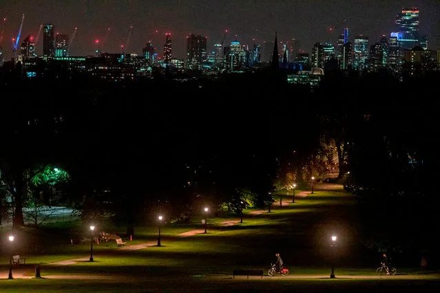 Cyclists take their daily exercise allowance through the park at night in Primrose Hill in London on April 18, 2020, during the novel coronavirus COVID-19 pandemic. The number of people in Britain who have died in hospital from coronavirus has risen by 888 to 15,464, according to daily health ministry figures on Saturday. (Photo by Justin Tallis/AFP Photo)