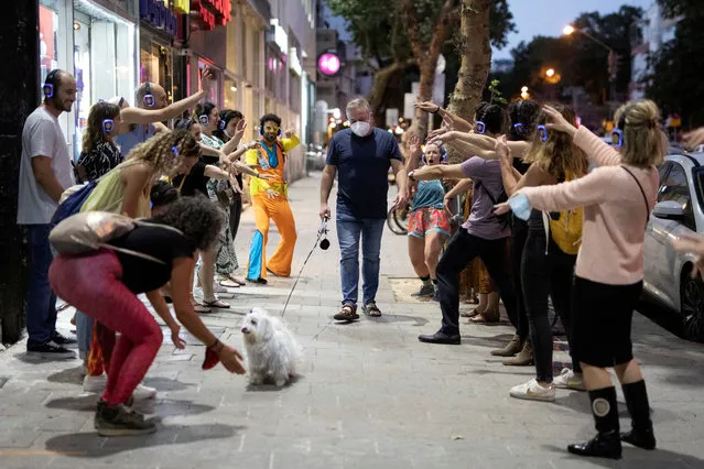 A man wears a mask and walks his dog past people taking part in a silent disco event as some businesses reopened at the end of last month under a host of new rules, following weeks of shutdown amid the coronavirus disease (COVID-19) crisis, in Tel Aviv, Israel on June 4, 2020. (Photo by Amir Cohen/Reuters)
