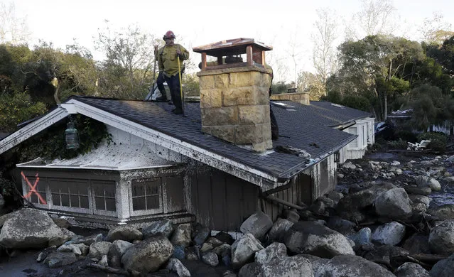 A firefighter stands on the roof of a house submerged in mud and rocks Wednesday, January 10, 2018, in Montecito, Calif. Anxious family members awaited word on loved ones Wednesday as rescue crews searched grimy debris and ruins for more than a dozen people missing after mudslides in Southern California destroyed houses, swept cars to the beach and left more than a dozen victims dead. (Photo by Marcio Jose Sanchez/AP Photo)