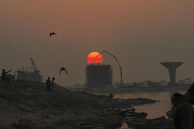 Laborers work at a construction site on the banks of river Ganges as the sun sets in Prayagraj, India, Thursday, December 22, 2022. (Photo by Rajesh Kumar Singh/AP Photo)