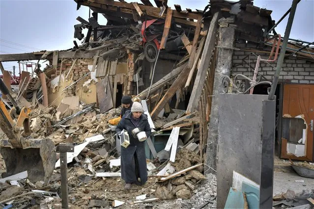 Local residents carry their belongings as they leave their home ruined in the Saturday Russian rocket attack in Zaporizhzhya, Ukraine, Sunday, January 1, 2023. (Photo by Andriy Andriyenko/AP Photo)