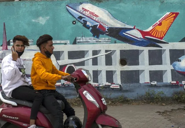 A scooterist drives past a wall painted with Air India planes in Mumbai, India, Thursday, January 27, 2022. India's oldest and largest conglomerate Tata Sons will merge its Air India with Vistara, which it jointly runs with Singapore Airlines, according to a statement released on Tuesday. (Photo by Rafiq Maqbool/AP Photo)