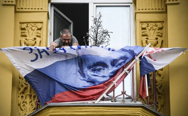 A man fixes a Russian campaign flag of President Vladimir Putin on the balcony of his apartment in Moscow on February  22, 2018. Russians will vote at the March 18 presidential election that Vladimir Putin is almost guaranteed to win. (Photo by Alexander Nemenov/AFP Photo)