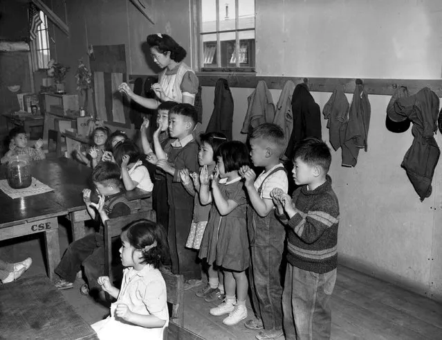 In this May, 1943 file photo, Aiko Sumoge, an assistant teacher, leads a Kindergarten class to sing an English folk song at the internment relocation center for Japanese Americans in Tule Lake, Ca., in during World War II. Roughly 120,000 Japanese immigrants and Japanese-Americans were sent to desolate camps that dotted the West because the government claimed they might plot against the U.S. Thousands were elderly, disabled, children or infants too young to know the meaning of treason. Two-thirds were citizens. (Photo by AP Photo/File)