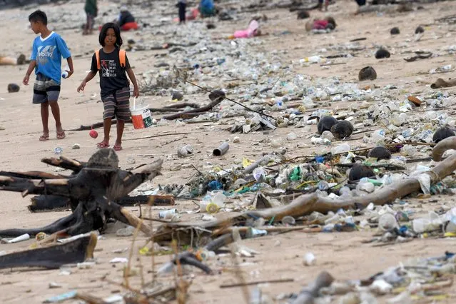 Children walk past plastic and other debris washed ashore at Kedonganan Beach, Badung regency, on Indonesia's resort island of Bali on April 12, 2023. (Photo by Sonny Tumbelaka/AFP Photo)