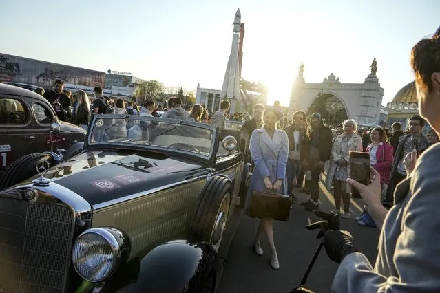 A woman dressed in the fashion of the middle of the last century poses in front of a ragged Mercedes issued in the early 40s, after a rally of retro cars during sunset at the VDNH, Exhibition of Achievements of National Economy, in Moscow, Russia, Sunday, April 23, 2023. The monument to the first Soviet rocket Vostok is in the background. (Photo by Alexander Zemlianichenko/AP Photo)