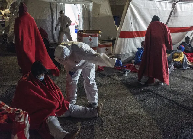 Rescued migrants sit inside a tent in the port of Arguineguin, Gran Canaria island, Spain, Saturday January 16, 2021. A Spanish rescue ship rescued a boat 160 kilometres south of Gran Canaria with men, women and children on board in very poor condition. (Photo by Javier Bauluz/AP Photo)