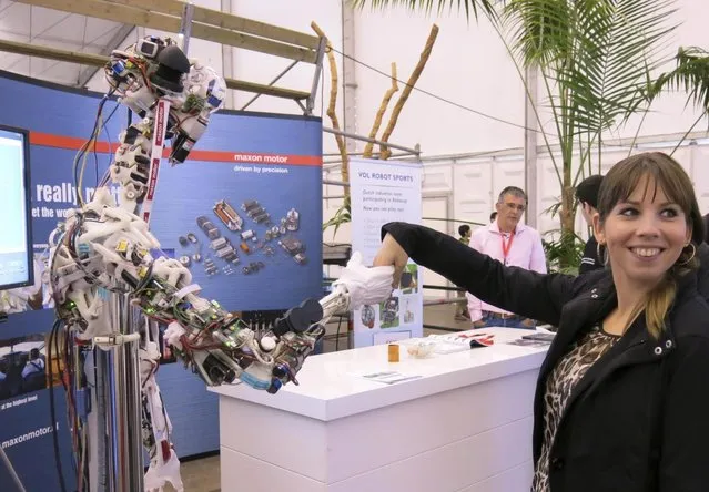 In this photo taken Thursday, June 27, 2013, a woman shakes hands with a robot at an exhibition outside the RoboCup championships in Eindhoven, Netherlands. Around 300 teams from 40 countries are competing this week in the RoboCup championships. The competition has the long-term goal of building a team of androids good enough to beat the human world cup team by 2050. (Photo by Toby Sterling/AP Photo)