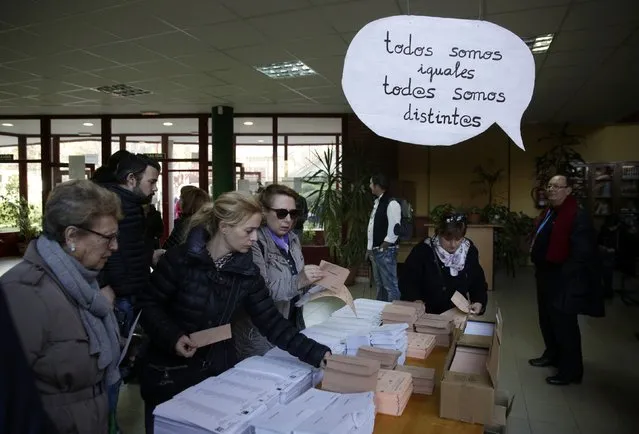 Voters select their ballots at a polling station with a sign hanging over the table which reads “We are all the same, we are all different” during voting in Spain's general election in Madrid, Spain, December 20, 2015. (Photo by Andrea Comas/Reuters)