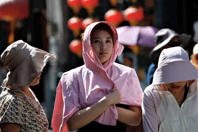 People wearing sun protection gear walk on a street, amid a red alert for heatwave in Beijing, China on July 6, 2023. (Photo by Tingshu Wang/Reuters)