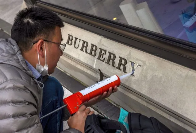 A man repairs damaged logo in front off the Burberry store in Shanghai, China, 26 March 2021. Burberry is the first luxury brand that suffered Chinese backlash over Xingjiang. International clothing brands Fila, Hugo Boss, H&M, Nike, and Adidas also experience consequences in China for refusing to buy Xinjiang cotton over claims of forced labor and genocide in the region. (Photo by Alex Plavevski/EPA/EFE)