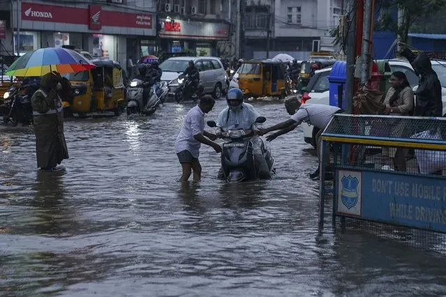 A traffic police officer, right and a man, left help a motorist at a water logged street during rain in Hyderabad, India, Thursday, July 20, 2023. India receives its monsoon rains from June to October. (Photo by Mahesh Kumar A./AP Photo)