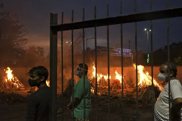People watch burning funeral pyres of their relatives who died of COVID-19 in a ground that has been converted into a crematorium in New Delhi, India, Thursday, May 6, 2021. Infections in India hit another grim daily record on Thursday as demand for medical oxygen jumped seven-fold and the government denied reports that it was slow in distributing life-saving supplies from abroad. (Photo by Ishant Chauhan/AP Photo)