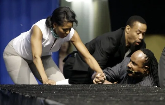 Michelle Obama (L) and singer Stevie Wonder (R) fall as they go up steps to the stage during a rally for Democratic presidential candidate US Senator Barack Obama (D-IL) at UCLA's Pauley Pavilion in Los Angeles, California, in this February 3, 2008 file photo. (Photo by Danny Moloshok/Reuters)
