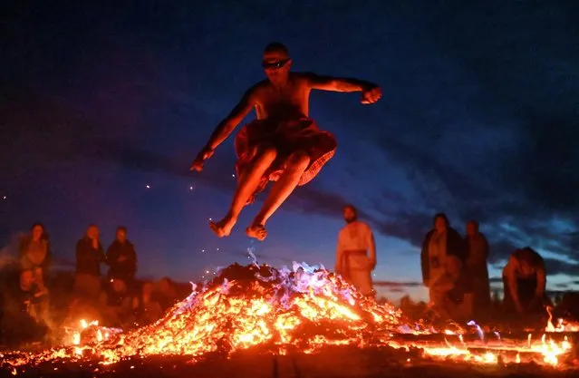 A man jumps over a bonfire during celebration of the summer solstice at a festival in the village of Okunevo in Omsk region, Russia on June 21, 2021. (Photo by Alexey Malgavko/Reuters)