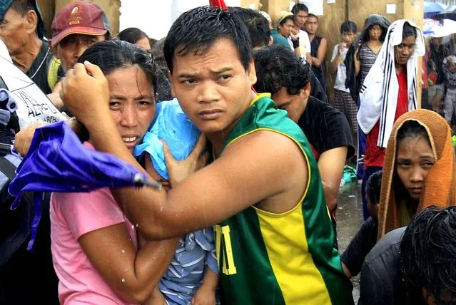 A husband and wife protect their baby from the rain as they wait for an evacuation flight in Tacloban, central Philippines, Tuesday, November 12, 2013. (Photo by Wally Santana/AP Photo)
