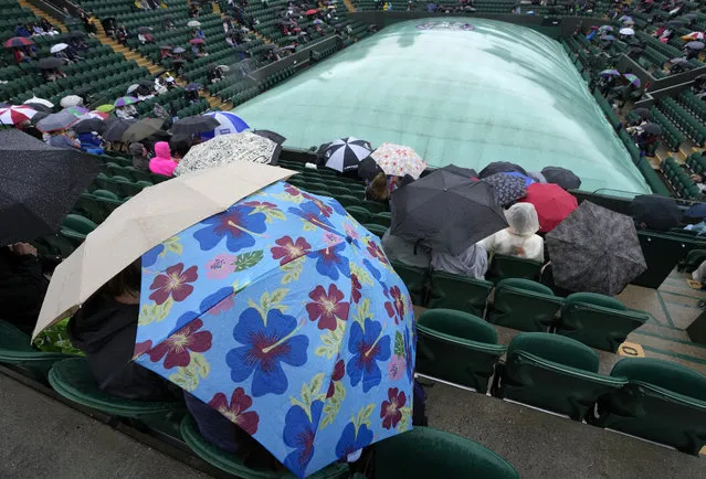 People shelter under umbrellas on Court 2 during a rain delay on day one of the Wimbledon Tennis Championships in London, Monday June 28, 2021. (Photo by Kirsty Wigglesworth/AP Photo)